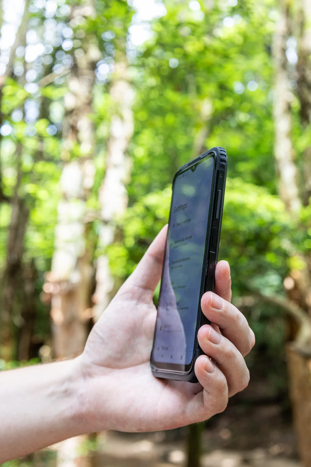 AGM H6 Pro mit eingeschaltetem Display, gehalten in einer Hand vor grünem Waldhintergrund