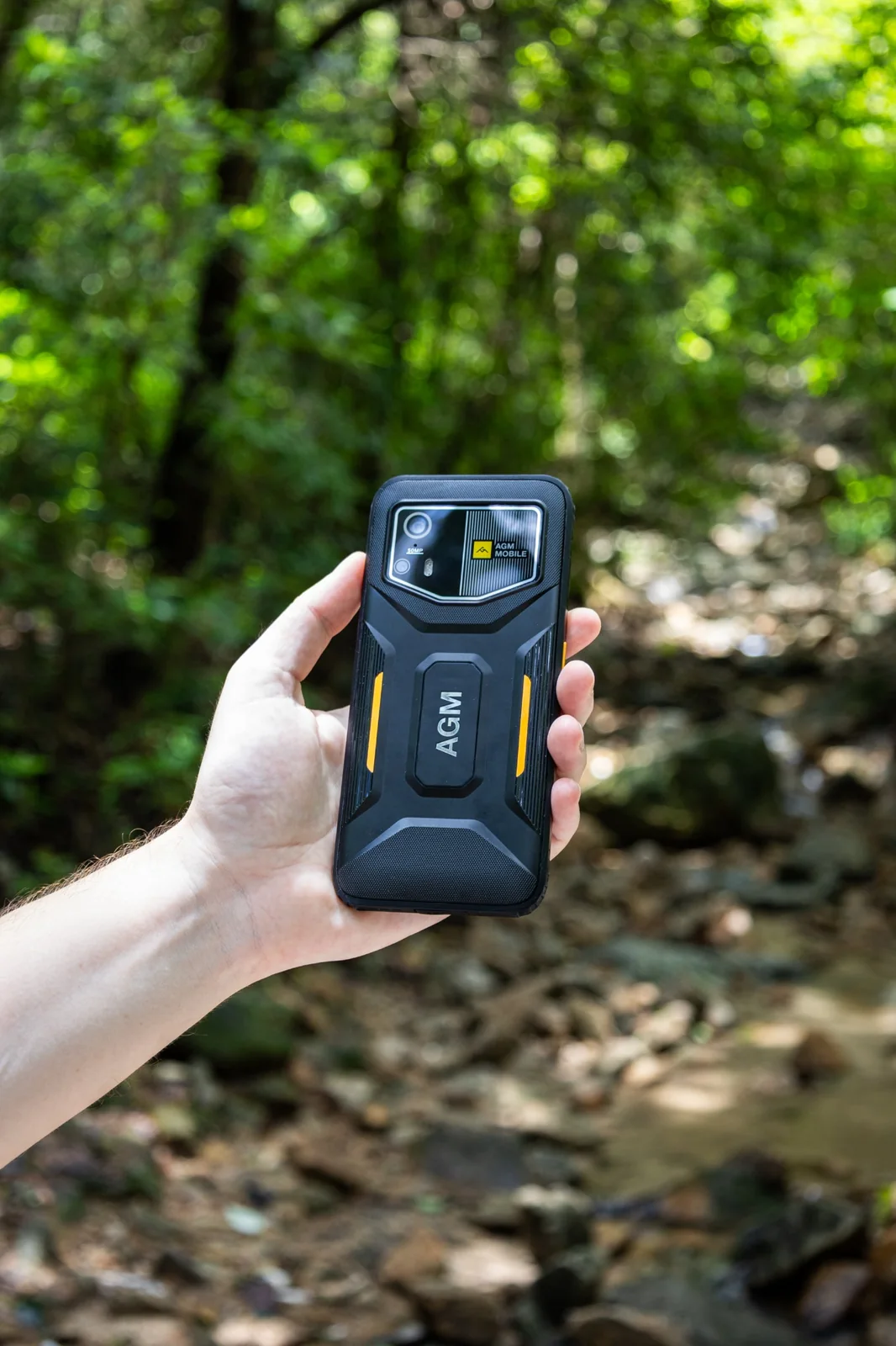 Rückseite des AGM H6 Pro mit Kamera und gelben Gehäuseakzenten, gehalten in einer Hand im Wald