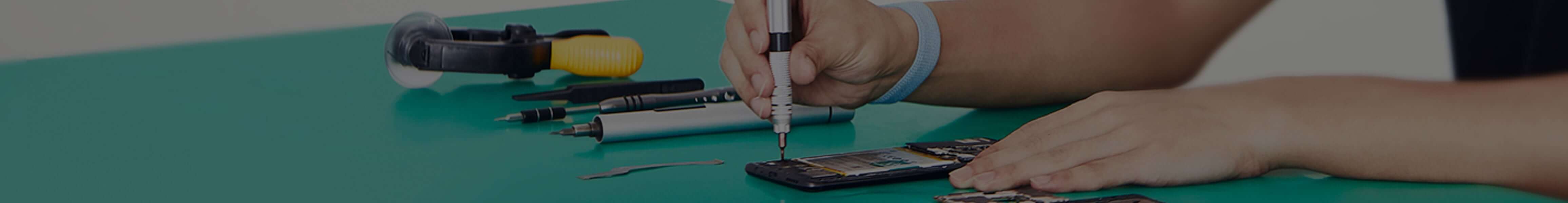 Techniker öffnet ein Smartphone mit Spezialwerkzeug auf einer Reparaturmatte